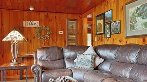 A cozy living room with a leather sectional sofa, a wooden table with a lamp, and a basket of pinecones.