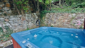 A hot tub with a stone wall backdrop, a control panel, and a hose.