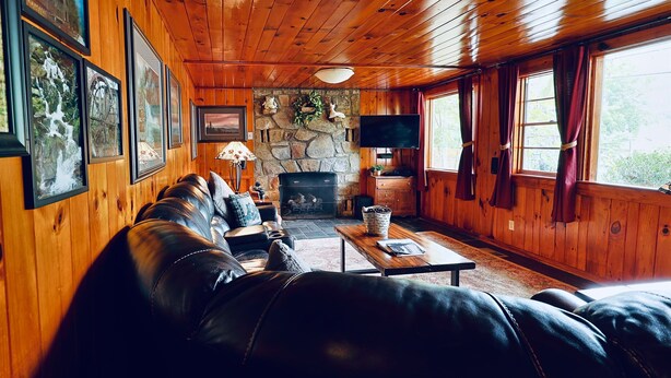 A cozy cabin interior with a stone fireplace, leather sofa, and framed pictures on the walls.