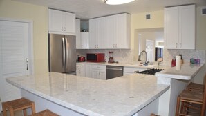 A kitchen with white cabinets, a stainless steel refrigerator, a microwave, and a sink. There are wooden stools at the island. - Island Life at its best (Key Largo)