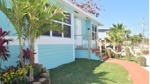 A light blue house with a wooden staircase leading to a front door, surrounded by a small lawn and various plants. - Island Life at its best (Key Largo)