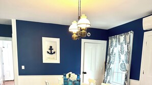 Une salle à manger aux couleurs bleu et blanc, avec une grande table, des chaises blanches et un tapis à motifs.