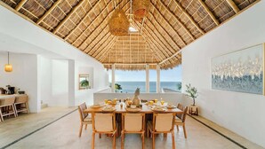 Un comedor con techo de paja, vista al mar y una mesa dispuesta para seis comensales.