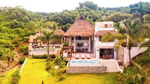 Una villa moderna con piscina, rodeada de exuberante vegetación y palmeras.