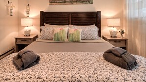 A neatly made bed with a patterned bedspread, two pillows with cactus designs, and two bedside lamps. - Desert Gardens #1 (Moab)
