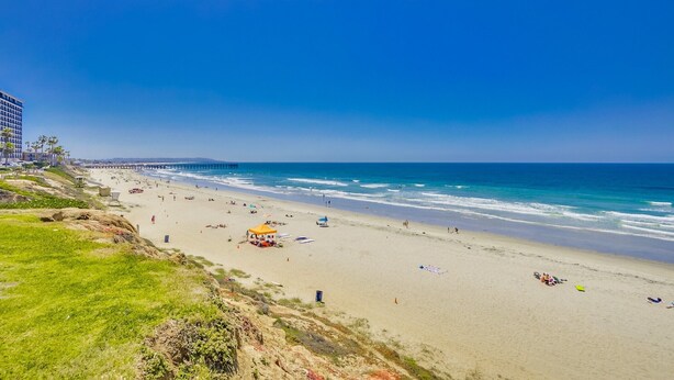 A beach with a pier extending into the ocean, sandy beach, and grassy areas. - Pacific Beach Townhome | 3BR w/ Hot Tub + Views (San Diego)