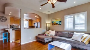 A spacious living area with a wooden floor, a gray sofa, a white coffee table, and a ceiling fan. - Pacific Beach Townhome | 3BR w/ Hot Tub + Views (San Diego)