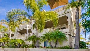 A multi-story hotel with balconies, palm trees, and a clear blue sky. - Pacific Beach Townhome | 3BR w/ Hot Tub + Views (San Diego)