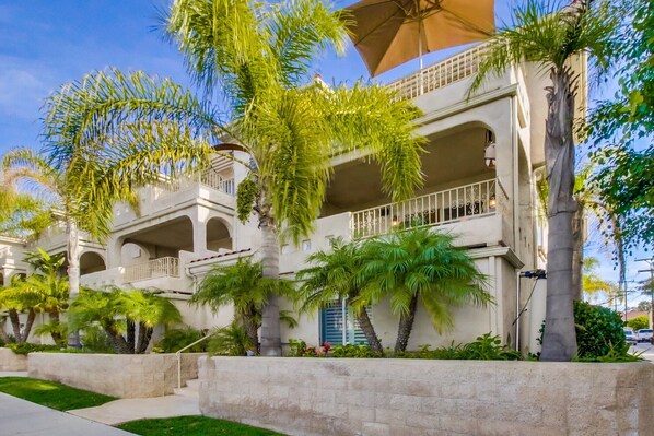 A multi-story hotel with balconies, palm trees, and a clear blue sky.