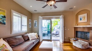 A living room with a sofa, ottoman, ceiling fan, and a fireplace. - Pacific Beach Townhome | 3BR w/ Hot Tub + Views (San Diego)