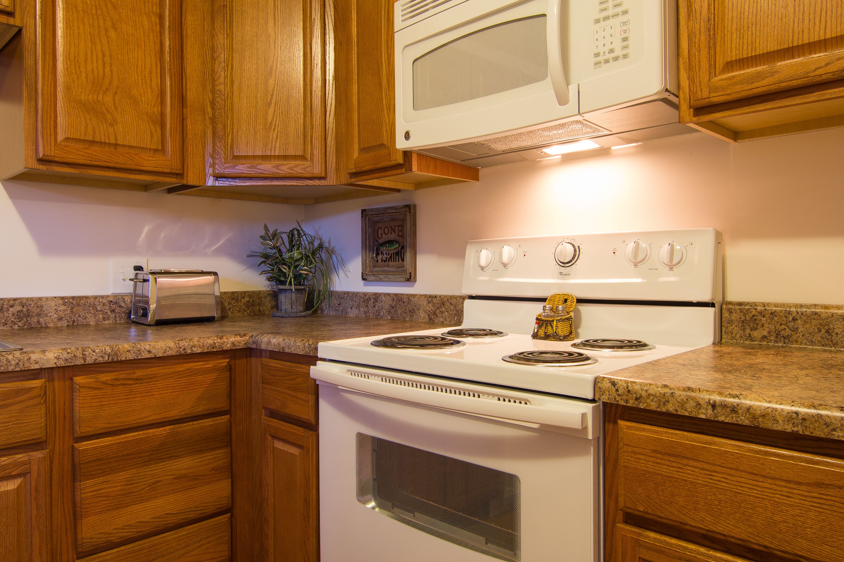 A kitchen with wooden cabinets, a white stove, a microwave, and a toaster on the counter.