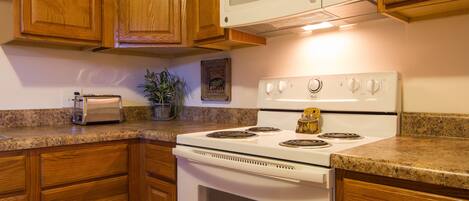 A kitchen with wooden cabinets, a white stove, a microwave, and a toaster on the counter.