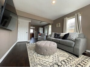Relax in this stylish living room with a tufted ottoman, sofa, and patterned rug.