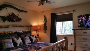 A cozy bedroom with a bed, a wooden headboard, a ceiling fan, a TV, a window with curtains, and a dresser. - Walk to The RIVER! Brand New 3 Bed/2 Bath. W/ FIRE PIT! (Sterling)
