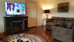 A living room with a fireplace, a television, a couch, and a rug. - Walk to The RIVER! Brand New 3 Bed/2 Bath. W/ FIRE PIT! (Sterling)