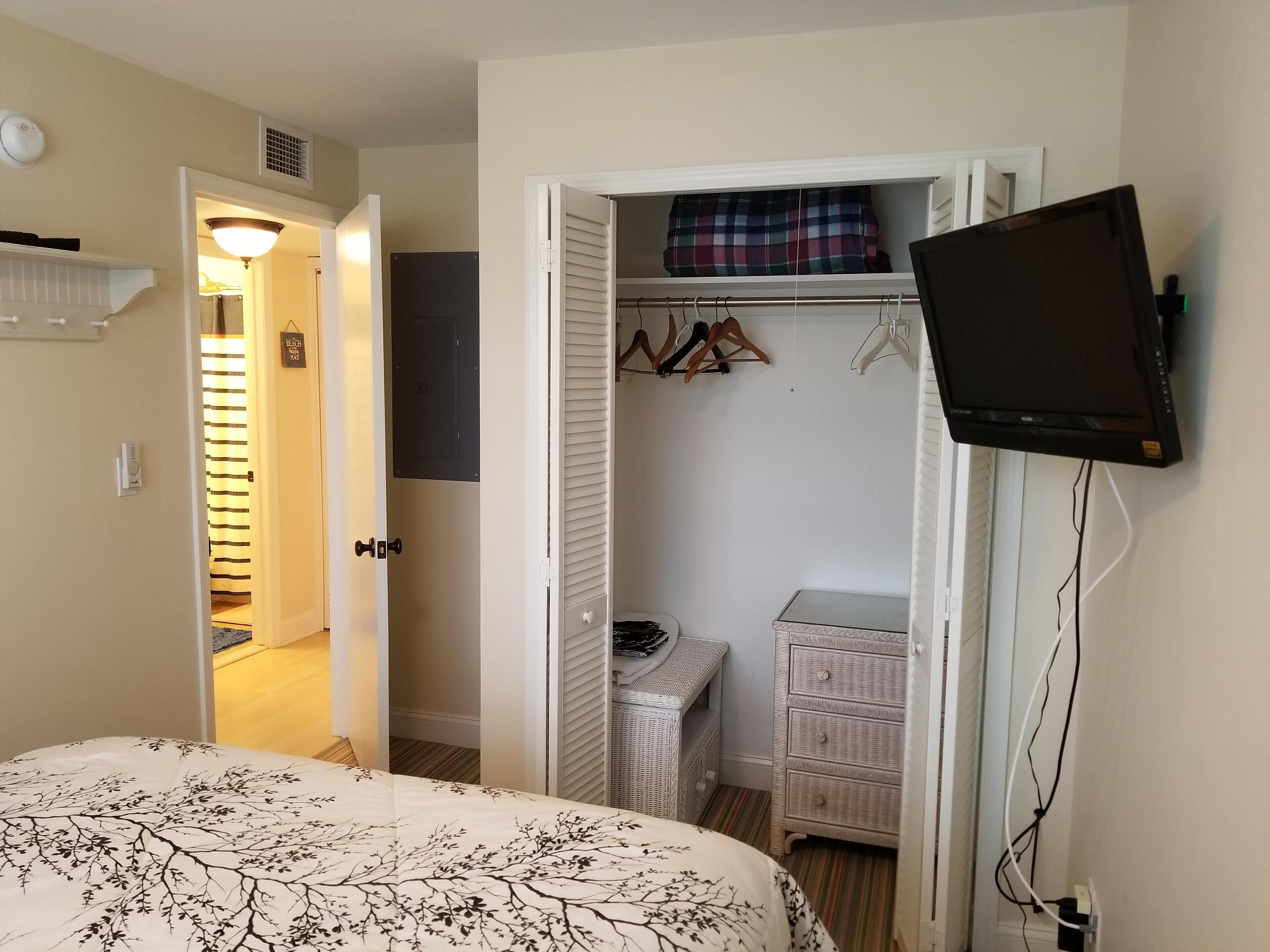 A bedroom with a bed, a television mounted on the wall, a wardrobe, and a small table.