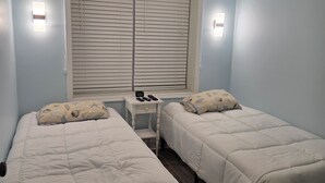 A bedroom with two beds, a bedside table with a lamp, and a window with blinds. - Cape May Condo Getaway w/ Rooftop Deck, Onsite Parking, 1/2 Block to the Beach (Cape May)