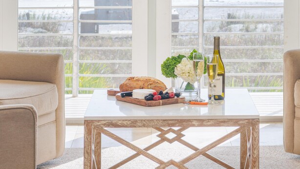 A balcony with a view of the ocean, a table with a loaf of bread, a bottle of wine, a glass, and a vase with flowers. - Oceanfront with Endless Ocean Views (Folly Beach)