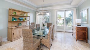 A dining area with a glass-top table surrounded by wicker chairs, a wooden buffet with glassware, and a chandelier. - Oceanfront with Endless Ocean Views (Folly Beach)