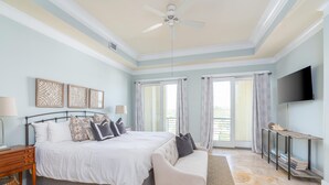 A bedroom with a large bed, bedside tables, a bench, a TV, and a bookshelf. - Oceanfront with Endless Ocean Views (Folly Beach)