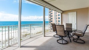 Un balcon avec vue sur la plage et l’océan, une table avec des chaises et une porte.