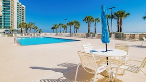 Un espace piscine doté d’une piscine à l’eau cristalline, de chaises longues blanches et d’un parasol bleu.