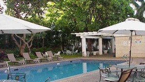 Una piscina con sillas de descanso y sombrillas, rodeada de vegetación.