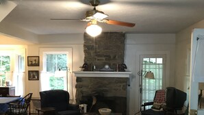 Una sala de estar acogedora con chimenea, ventilador de techo y comedor con mesa y sillas.
