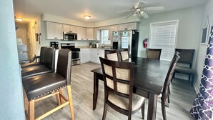 A modern kitchen with white cabinets, stainless steel appliances, and a dining area with dark wooden furniture.