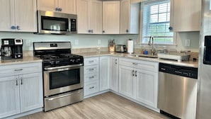 A modern kitchen with light wood cabinets, stainless steel appliances, and a window providing natural light.