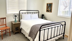 Un dormitorio con una cama, una mesita de noche, una silla, una lámpara de pie y un cuadro en la pared.