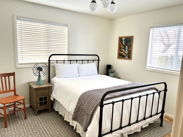 A bedroom with a bed, a nightstand, a chair, a floor lamp, and a painting on the wall.