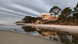A beachfront property with a large house, a reflective water body, and surrounding vegetation. - Beachfront, kid friendly seas, seclusion, nature (Carrabelle)