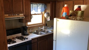 Une cuisine de taille réduite, avec des meubles de rangement en bois, un réfrigérateur blanc, une cuisinière et un évier.