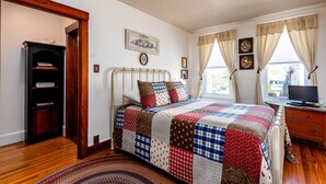 A bedroom with a quilted bedspread, wooden floor, a bookshelf, a desk with a television, and a window with curtains. -  Lincoln Quarters, 2nd floor,  Only 2 blocks to the center of town. (Gettysburg)