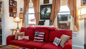 A red sofa with American flag pillows, a framed picture of a man with a guitar, and a window with curtains. -  Lincoln Quarters, 2nd floor,  Only 2 blocks to the center of town. (Gettysburg)