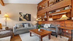 A cozy living room with a grey sofa, a wooden coffee table, and a bookshelf filled with books and decorative items. - RMR: Thistle 921 Condo in The Aspens/Wilson,WY (Wilson)