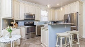 A modern kitchen with white cabinetry, stainless steel appliances, a marble countertop, and a small dining area with stools. - HISTORIC DISTRICT ~ Free Parking! (Saint Augustine)