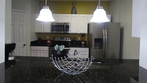 A kitchen with white cabinets, a black countertop, a stainless steel sink, and two pendant lights.