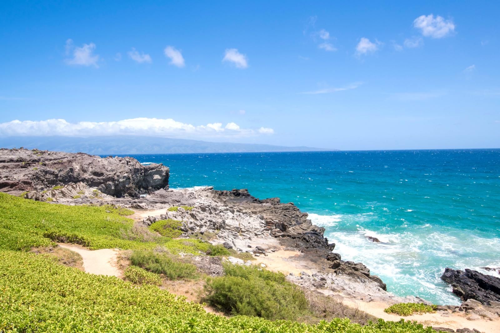 A coastal landscape with rocky terrain, a clear blue sky, and the ocean.