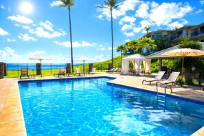 A swimming pool with lounge chairs and umbrellas, a stone fence, and a view of the ocean.