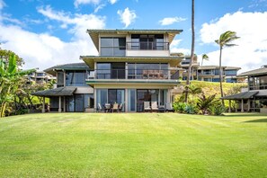 A multi-story residential building with a large front lawn, a covered patio, and a view of the surrounding neighborhood.