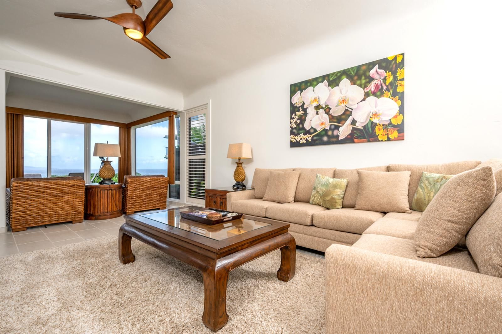 A living room with a sofa, coffee table, and a painting of orchids.