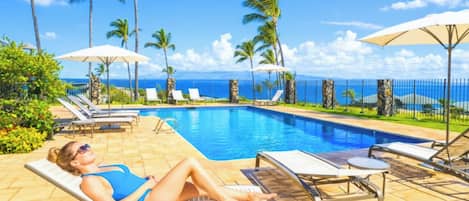 A poolside area with lounge chairs, umbrellas, and a view of the ocean.
