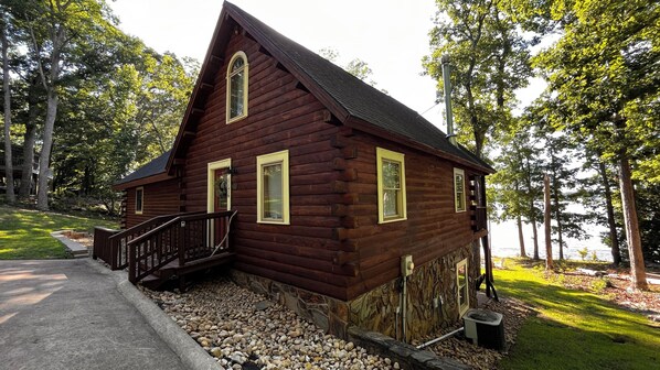 A wooden cabin with a stone foundation, a wooden deck, and a view of a lake. - Waterfront Cozy Log Cabin Lake House - The Sunset Cabin (Leesville)