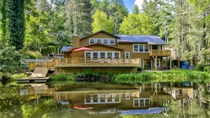 A two-story lodge with a deck and a covered porch, situated by a calm lake with dense forest in the background. - Location, Location, Location. (Highlands)
