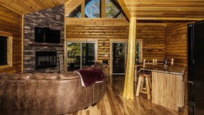 Ein Blockhaus-Interieur mit Kamin aus Stein, einer Ledersofa, einem Holzesstisch und einer Küchenzeile.