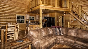 Ein Holzblockhaus-Interieur mit einer Holztreppe, einem Ledersofa und einem Essbereich.