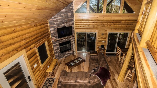 Ein Blockhaus-Interieur mit Kamin aus Stein, einem großen Sofa und einem Essbereich.