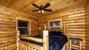 Ein Zimmer in einer Holzhütte mit einem Bett, einem Deckenventilator und einem Fenster mit Jalousien.
